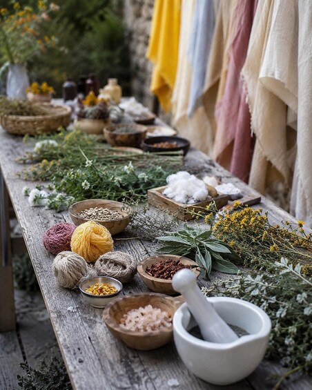 A rustic outdoor setting with a wooden table filled with various herbs, spices, and a mortar and pestle. 3