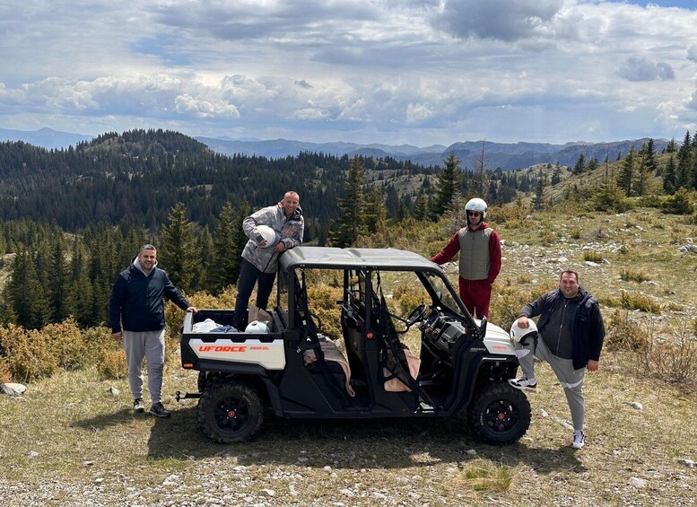 A group of people standing next to a utility vehicle on a grassy hillside with a mountainous backdrop. 2