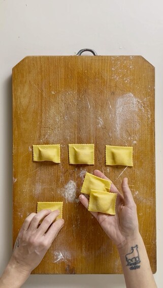 Hands placing ravioli on a wooden board. 4