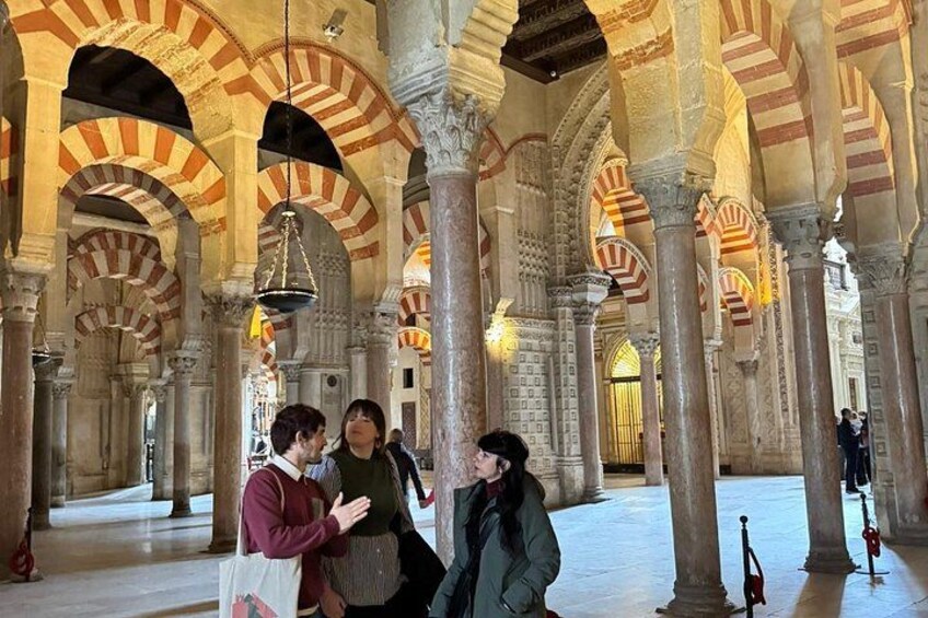 A historic building with arches and columns, interior lighting, and a group of people. 2