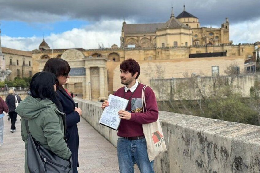A person holding a map and a bag, standing on a bridge with a historic building in the background. 3