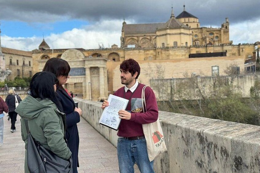 A person holding a booklet and a bag, standing on a bridge with a historic building in the background. 3