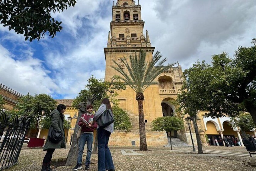 A historic building with a bell tower, palm trees, and a cobblestone courtyard. 4