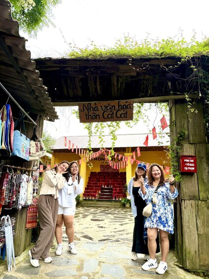 A group of people posing in front of a traditional market entrance with a sign reading 'Nhà văn hoa thôn Cát Cat.' 5