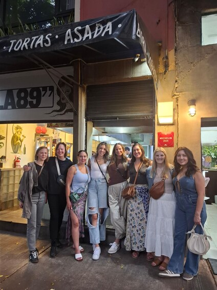 A group of people standing in front of a restaurant named 'Tortas Asada.' 2