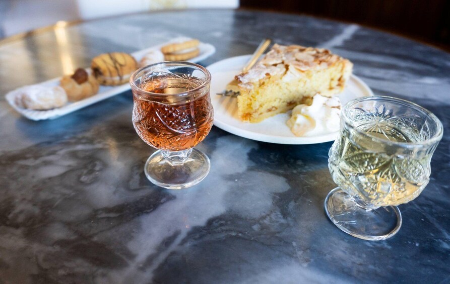 A marble table with a slice of cake, a glass of amber liquid, and a glass of clear liquid. 5