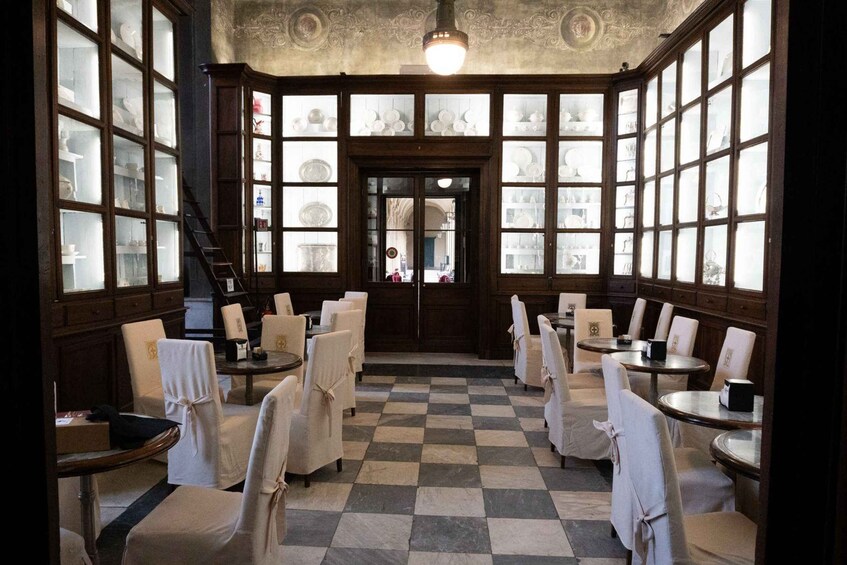 A dining area with checkered flooring, white chairs, and a central staircase. 2
