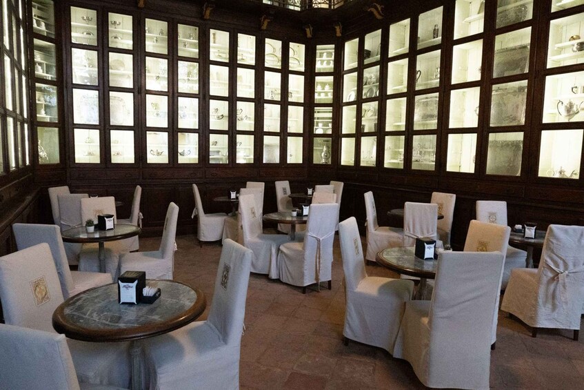 A room with multiple tables and chairs, large windows with glass panes, and a stone floor. 3