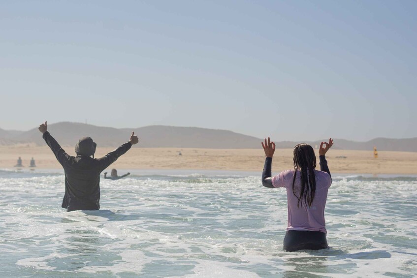 Two people in the ocean with their arms raised, a beach, and distant hills. 2
