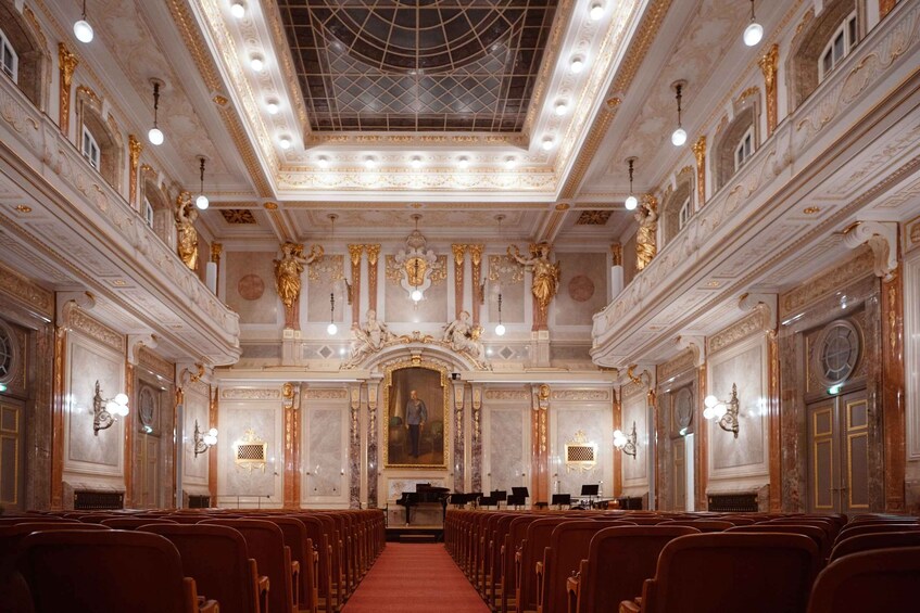 An ornate hall with a central stage, rows of chairs, and classical statues. 2