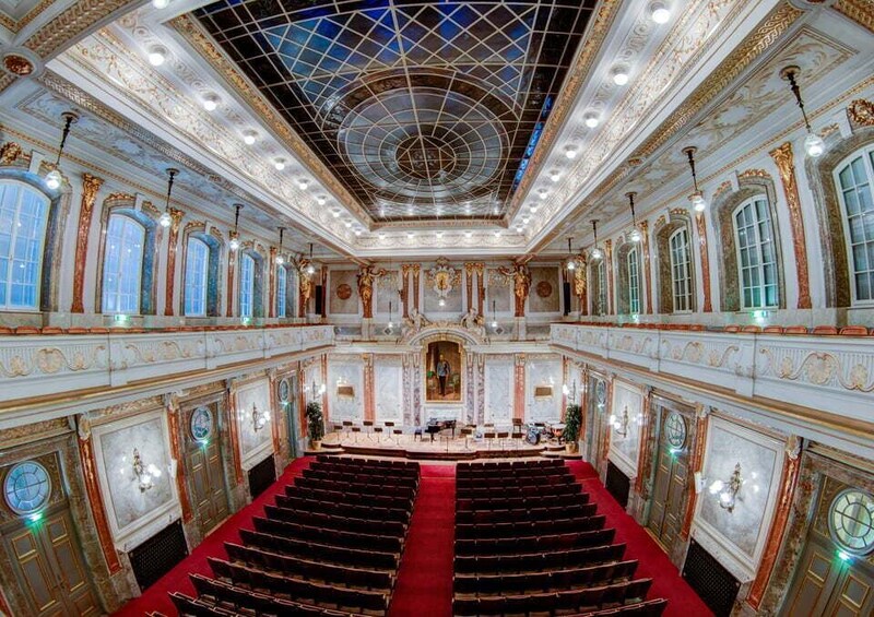 An ornate theater with a red carpet, rows of seats, and a detailed ceiling. 1