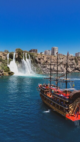 A boat with passengers, a waterfall, and buildings in the background. 1