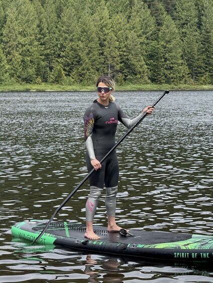 A person paddleboarding on a lake with a forest in the background. 5