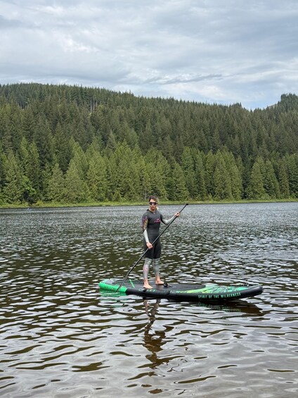 A person paddleboarding on a lake with a forested mountain in the background. 2