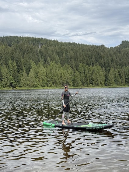 A person paddleboarding on a lake with a forested hill in the background. 1
