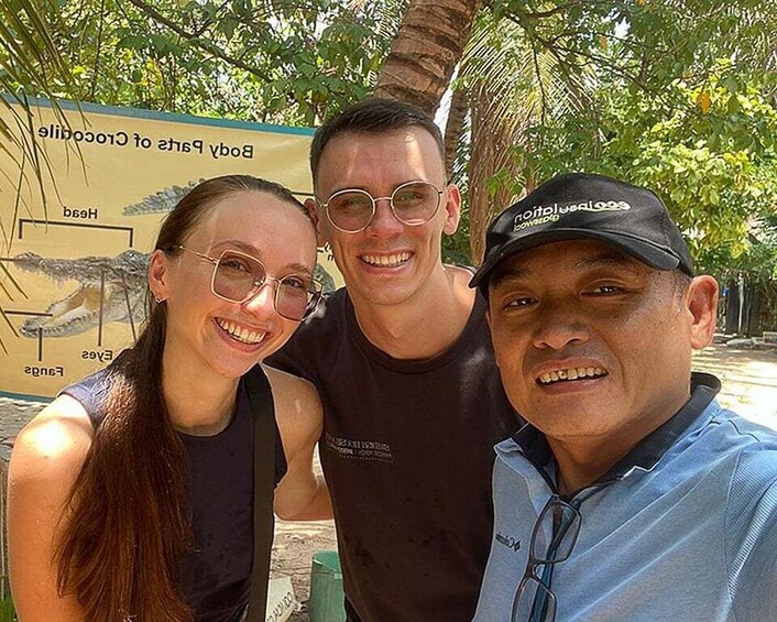 Three people posing in front of a sign with a crocodile illustration. 5