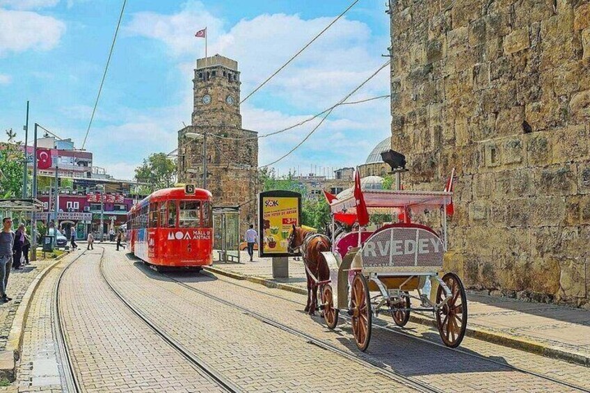A red tram, a horse-drawn carriage, and a stone tower in a historic town. 1