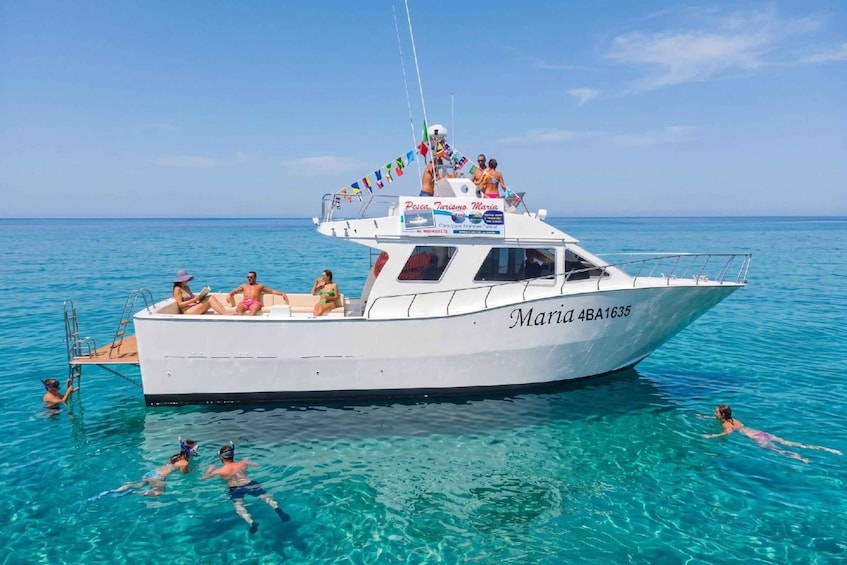 A white boat named 'Maria 4BA1635' on clear blue water with people swimming and snorkeling. 1