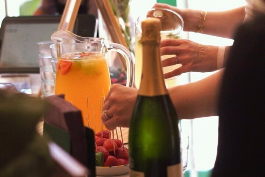A person pouring a drink from a bottle into a glass, with a pitcher of orange juice and strawberries in the background. 4
