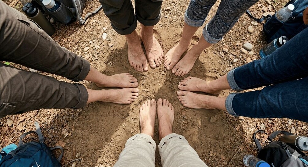 A group of people standing in a circle with their feet together on a dirt ground. 4