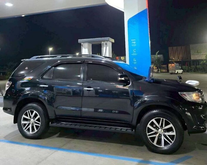 A dark-colored SUV parked at a gas station with a blue pillar and a white van in the background. 5