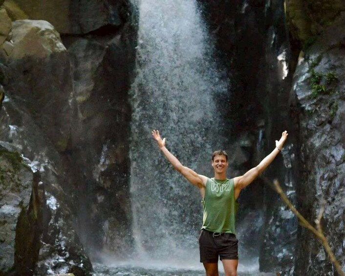 A person standing with arms raised in front of a waterfall. 1