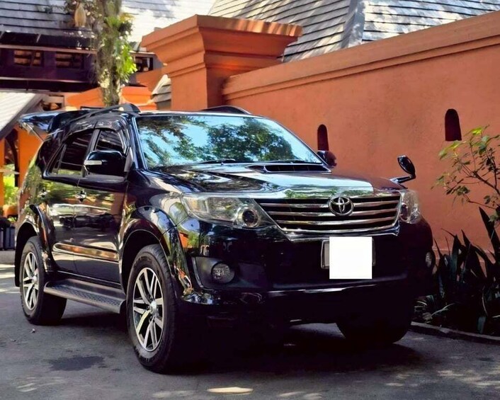 A black Toyota SUV parked in front of a house with a red wall and a window. 3