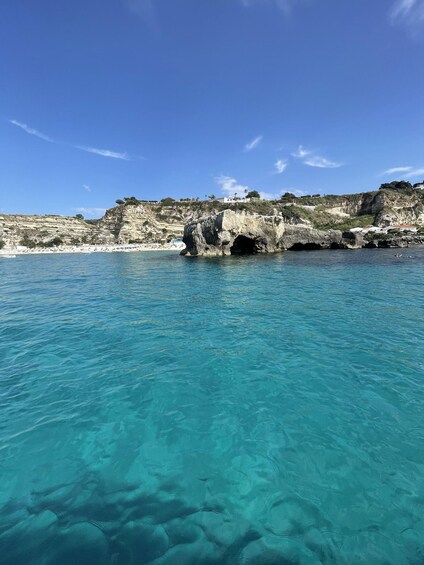 A coastal landscape with clear turquoise waters, rocky cliffs, and a sandy beach. 4
