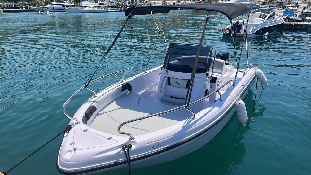 A small, white motorboat with a canopy, docked at a marina with other boats. 1