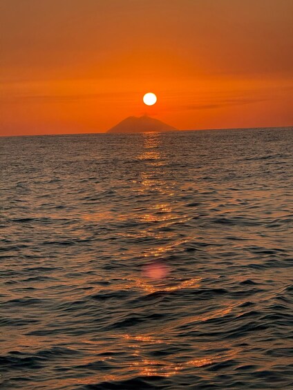 A sunset over the ocean with a mountain silhouette in the distance. 3