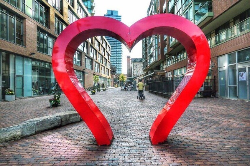 A red heart-shaped sculpture in an urban setting with buildings and a cobblestone street. 3