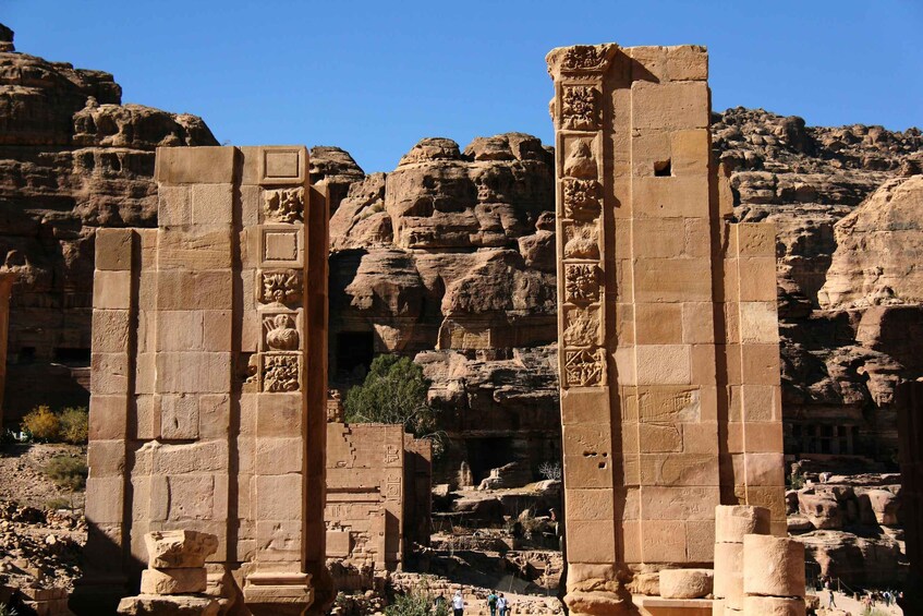 Ancient sandstone columns with carvings, set against a rocky cliff backdrop. 2