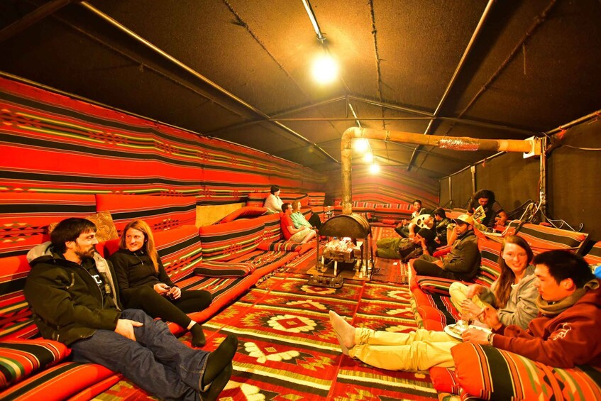 A group of people sitting on colorful, patterned floor mats in a tent-like structure. 3