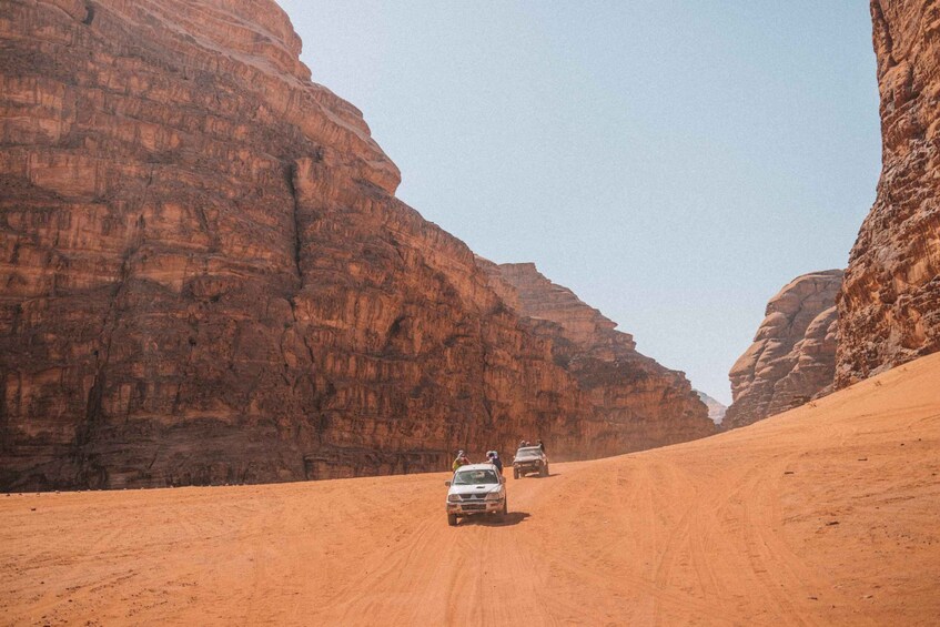 A desert road flanked by red rock cliffs with vehicles driving on it. 5