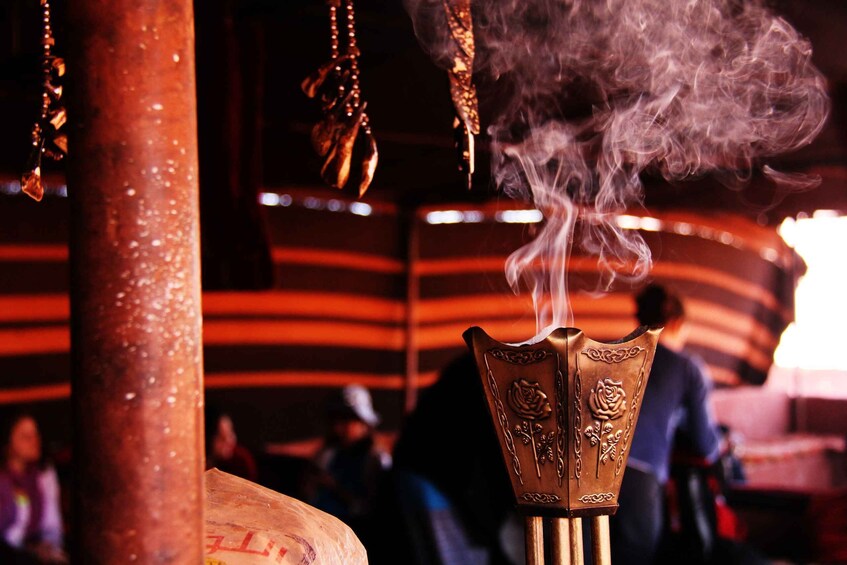 A ceremonial object with smoke rising, a decorative pillar, and a blurred background with people. 4