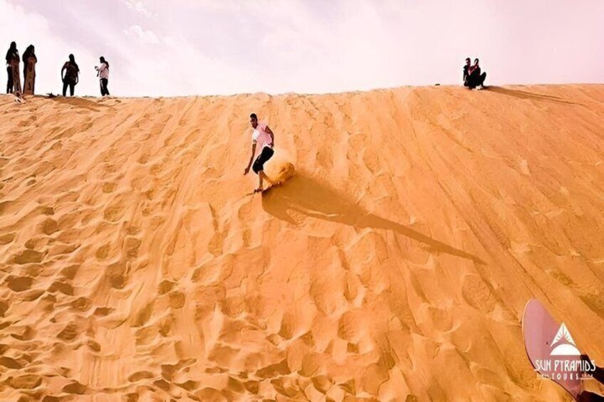 A person sliding down a sand dune with others standing in the background. 5