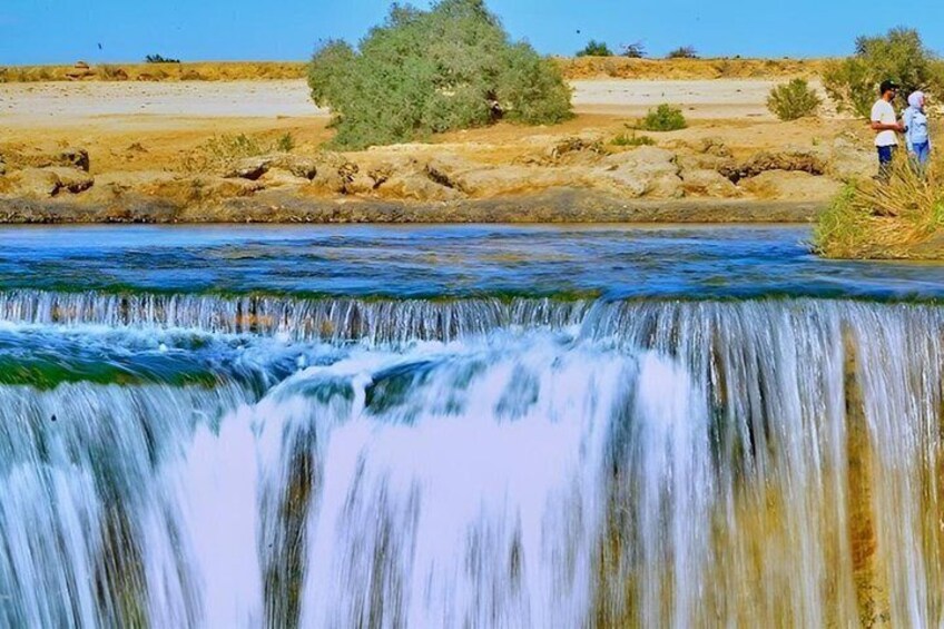 A waterfall in a dry riverbed with people observing it. 3