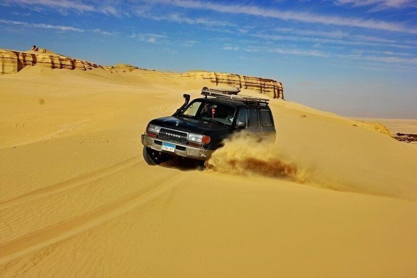 A black SUV driving through a desert with sand dunes in the background. 1