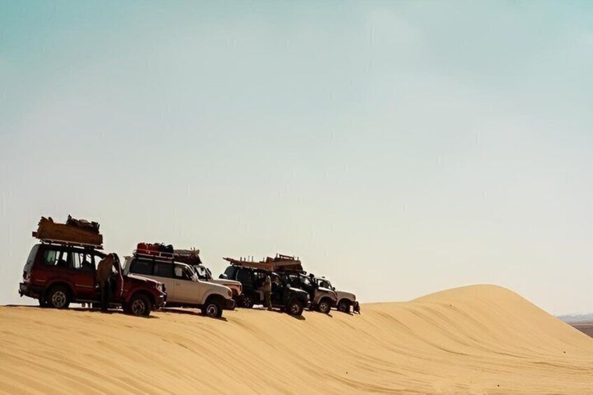 A convoy of off-road vehicles parked on a sand dune. 2