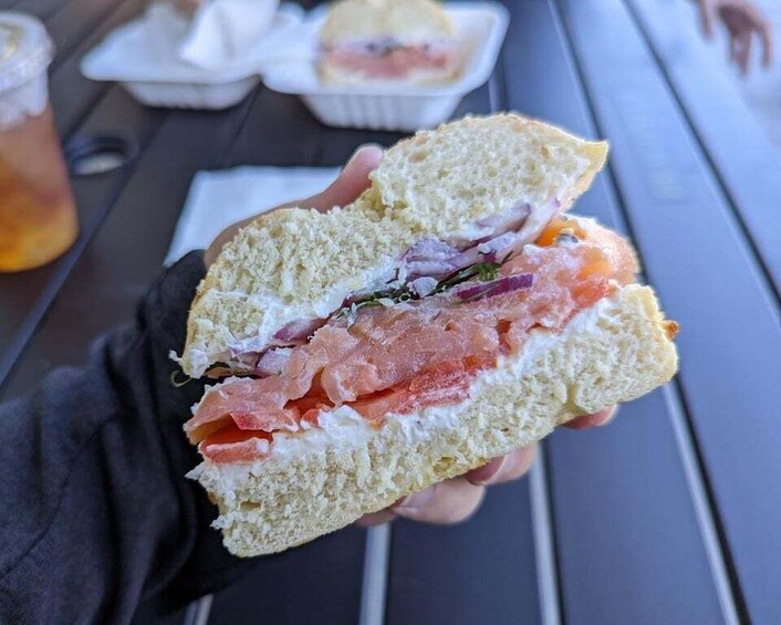 A person holding a sandwich with visible layers of meat and vegetables. 1