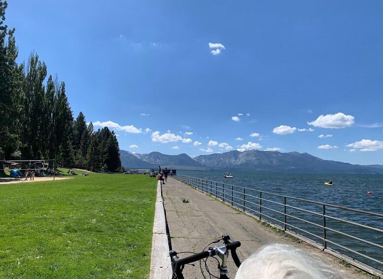A lakeside path with a bicycle, people walking, and boats on the water. 4