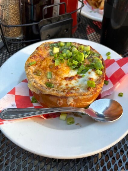 A bowl of soup with green onions on a white plate with a red and white checkered paper underneath. 5