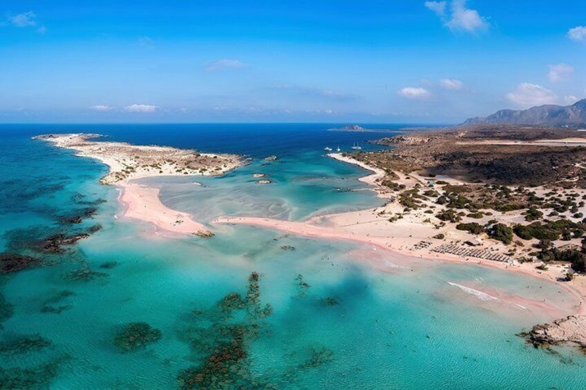 A coastal landscape with clear turquoise waters, a sandy beach, and a distant mountain range. 1