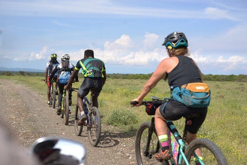 A group of cyclists on a dirt road with a grassy field and distant mountains in the background. 3