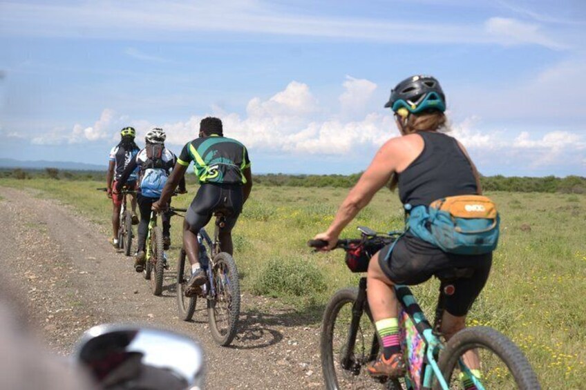 A group of cyclists on a dirt road with a grassy field and distant mountains in the background. 3