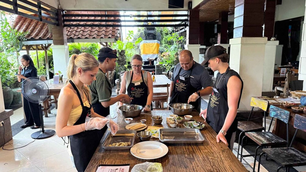 A group of people preparing food in an outdoor kitchen area with wooden tables and a tiled roof. 3