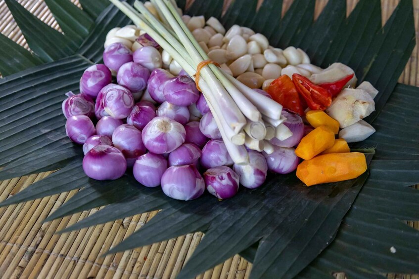 A variety of fresh vegetables including purple onions, garlic, red and yellow peppers, and ginger, arranged on a bamboo mat. 4