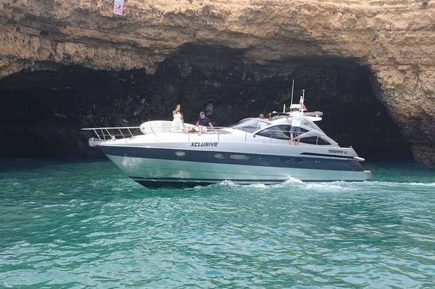A yacht named 'Xclusive 55' with passengers, sailing near a rocky coastline. 1