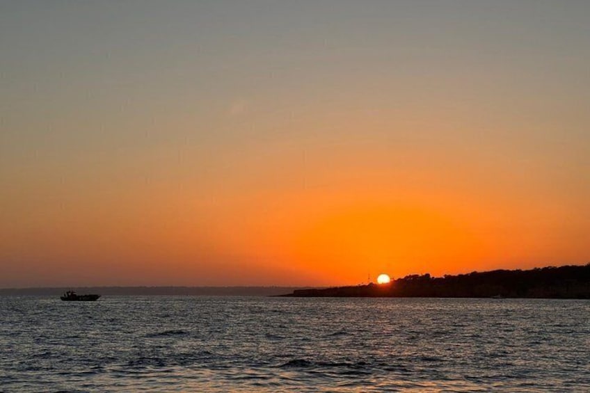 A sunset over a calm sea with a boat and a distant shoreline. 2