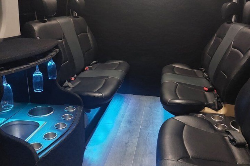A car interior with black leather seats, a center console with cup holders, and blue ambient lighting. 1